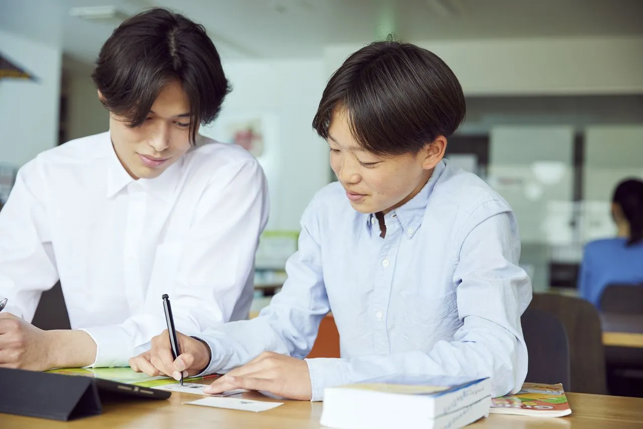 バイリンガル教師と中学生が一緒に英語を書いている様子